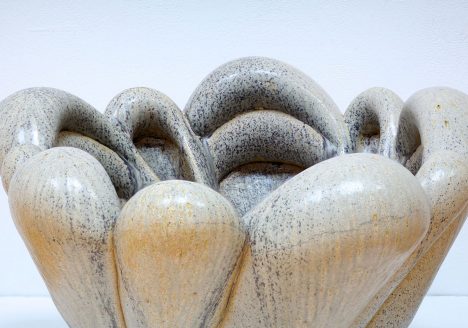 ceramic vessel of arched, bulbous shapes, glazed a pale brown with black and orange speckles.