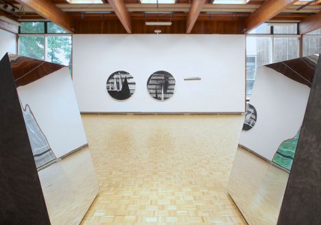 usdan gallery with several works by Torkwase Dyson: two circular canvases and sculptural work of two quadrilateral prisms with one side that is a mirror facing each other.