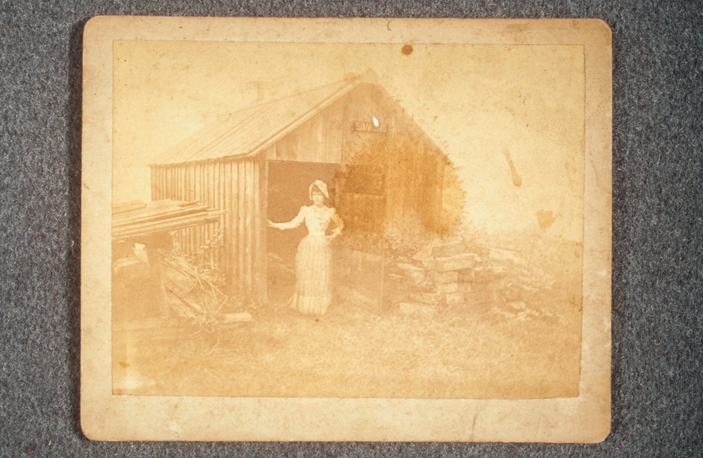 unknown. Seton, standing in the doorway of a shed. Above the doorway, a sign says "Simmons.". 1880s. Artstor,